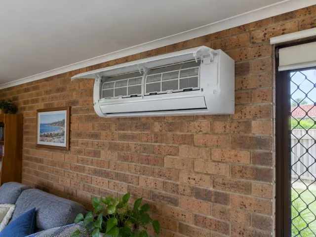 Clean split system indoor unit with open front panel and visible filters on a brick wall in a living room in Merrimac