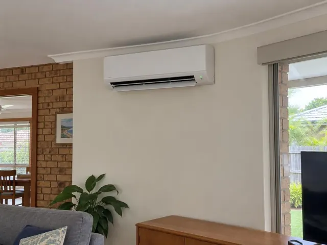 Wall-mounted split system on a white living room wall with louvre open in a brick and timber home in Mermaid Waters