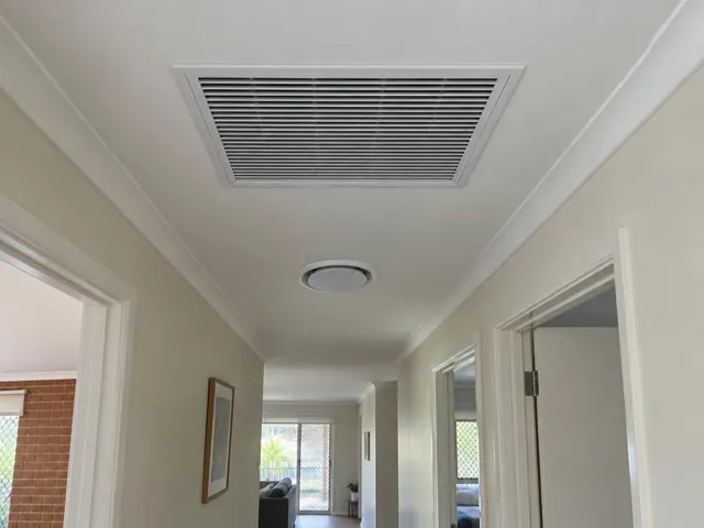 Ceiling return-air grille and round vent in a light hallway with open doorways in Mermaid Waters